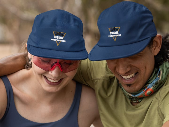 Two happy outdoor enthusiasts wearing 'Peak Performers' branded caps, sharing a light moment together. The image captures the spirit of adventure and camaraderie, perfect for a rock climbing group or outdoor gear brand.