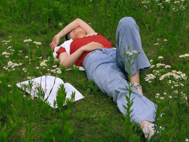 frühjahrsmüdigkeit tipps, frau liegt auf wiese im frühling