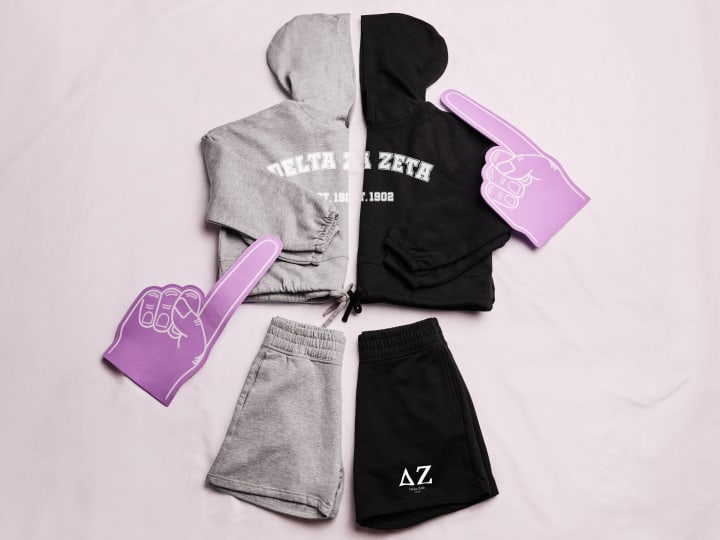 Matching sorority sets including hoodies and shorts with Greek letters, displayed with Greek-themed foam hands.