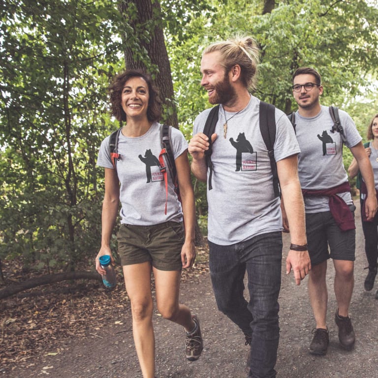 Uomo e donna sorridenti che indossano t-shirt personalizzate con scritte e grafiche originali davanti a un lago.