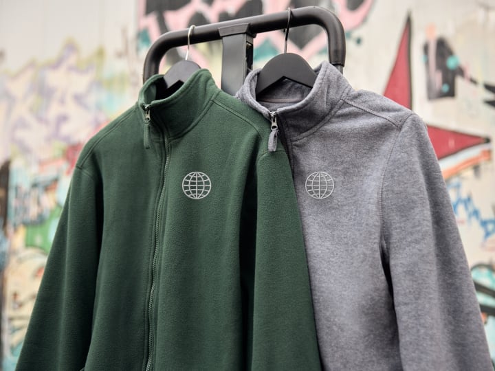 Due giacche sportive con zip in verde scuro e grigio appese ad un appendiabiti.