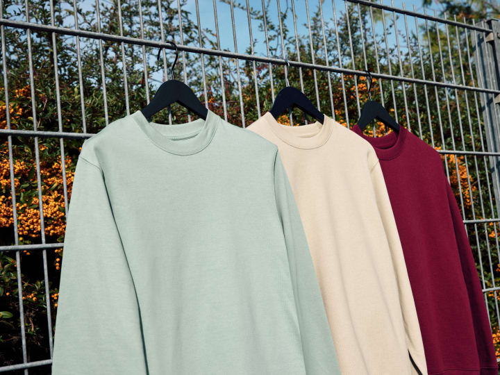 Tre felpe girocollo di diversi colori appese ad una recinzione