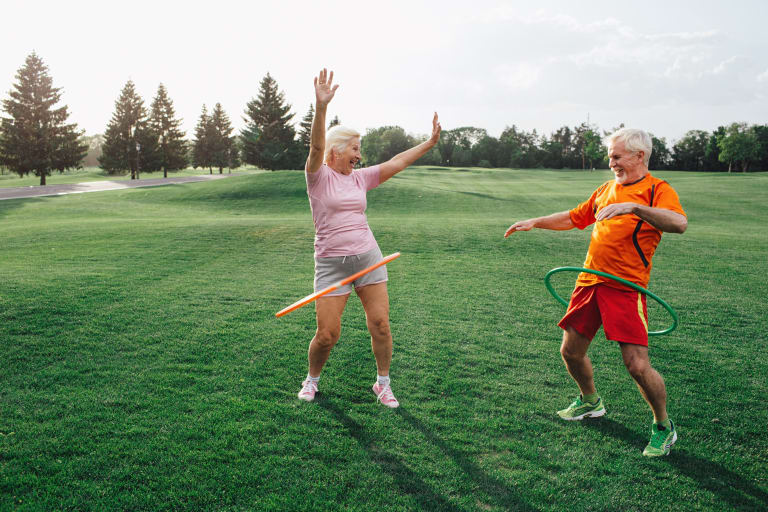 sport für zuhause, älteres ehepaar draußen beim hula hoop