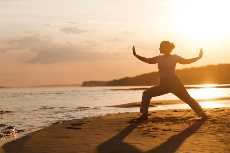 sport für zuhause, frau bei qigong am strand im sonnenuntergang